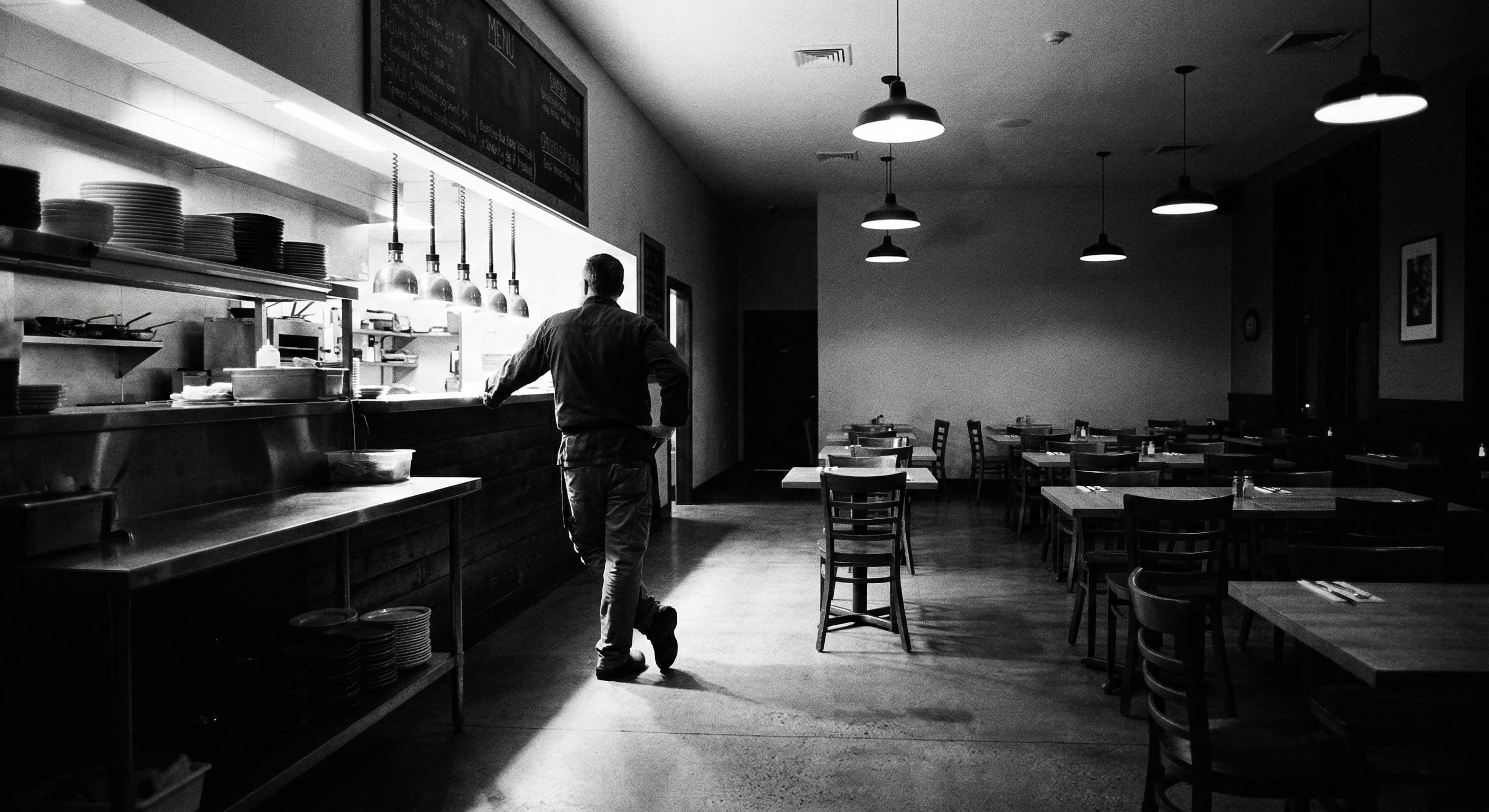 Restaurant operator standing at the pass in an empty dining room