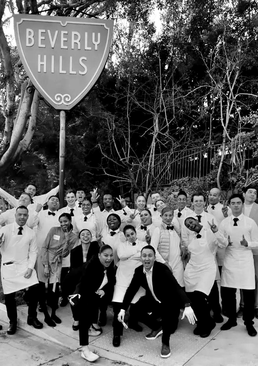 An opening team in white service jackets and aprons, arms raised, gathered under the Beverly Hills city shield sign